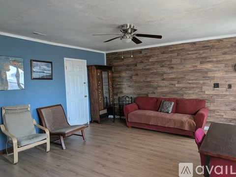 A living room with a red couch, a chair, and a wooden wall.