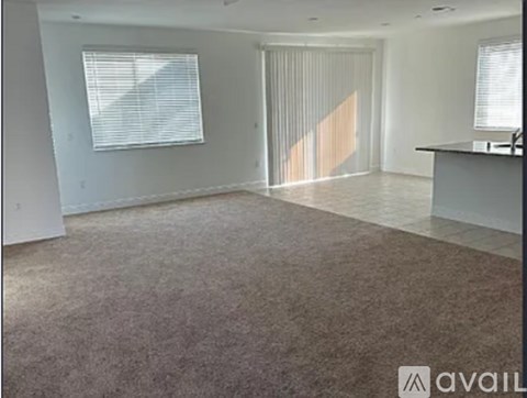 A spacious room with a carpeted floor and a large window with blinds.