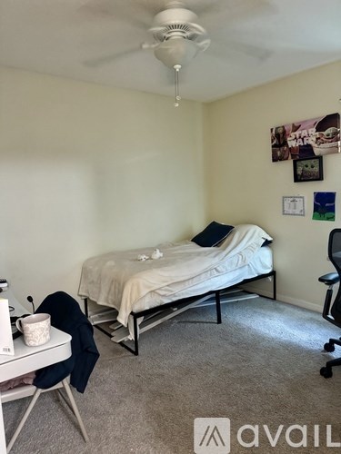 A bedroom with a bed, desk, chair, and ceiling fan.