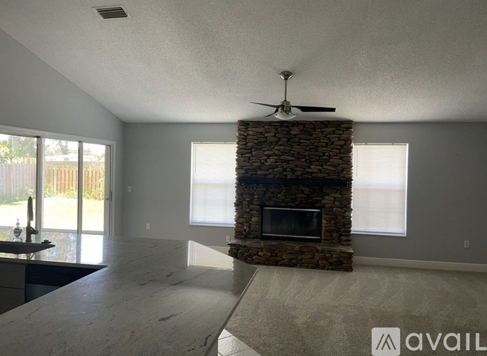 A living room with a stone fireplace and a fan on the ceiling.