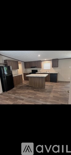 A kitchen with wooden flooring and a black refrigerator.