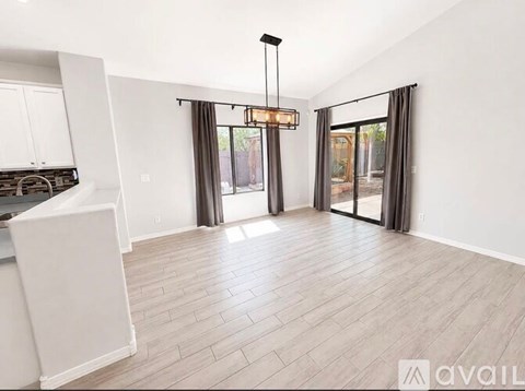 A spacious living room with a kitchen area to the left and a sliding glass door leading to a balcony.