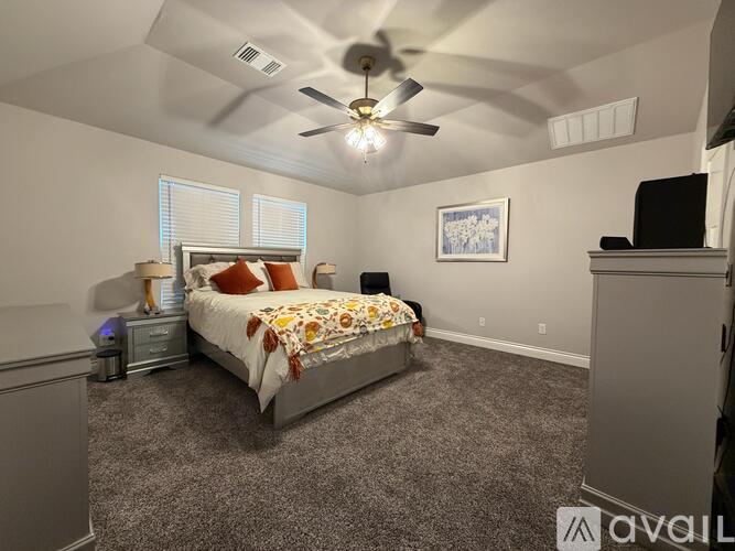 A bedroom with a bed, a ceiling fan, and a painting on the wall.