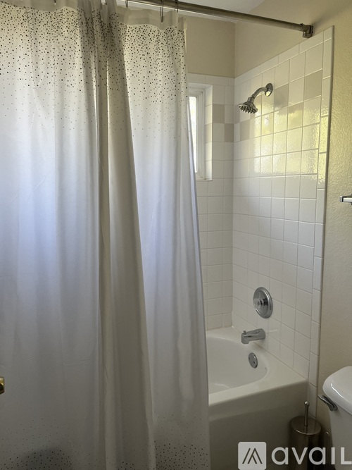 A white shower curtain with silver dots is hanging in a white tiled bathroom.
