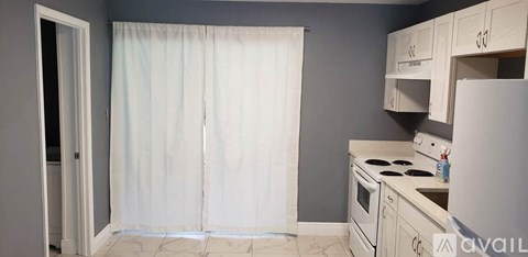 A kitchen with a white stove top oven and white cabinets.