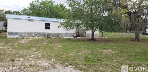 A white metal building with a blue roof is surrounded by a grassy area and trees.