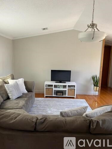 A living room with a grey sofa and a television on a white stand.