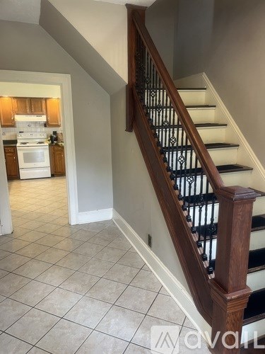 A staircase with a wooden handrail and black metal balusters leads to a kitchen.
