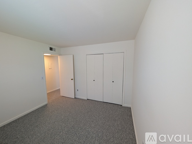 A room with grey carpet and three white cupboards.