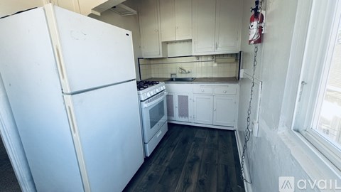 A white refrigerator is in a kitchen with wooden floors.