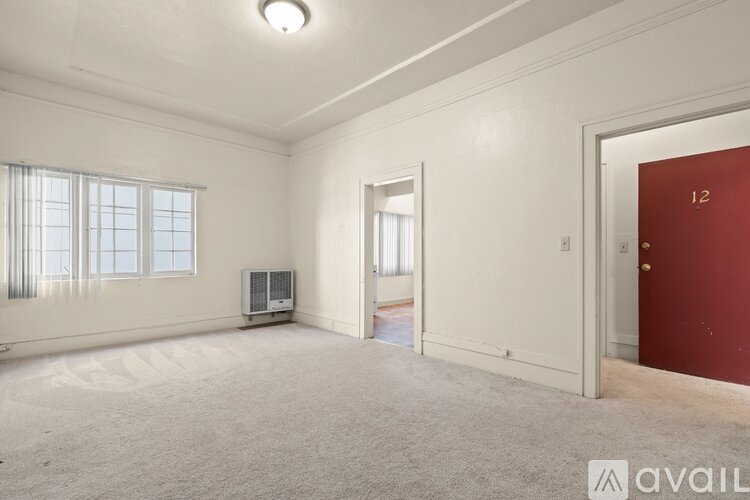 A room with a red door labeled 12 is empty and carpeted.