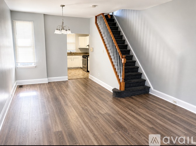 A wooden staircase with a black carpeted stair runner leads up to a kitchen area.