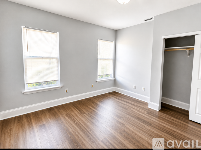 A room with wooden flooring and two windows.
