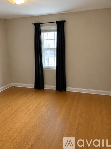 A room with wooden flooring and a window with black curtains.