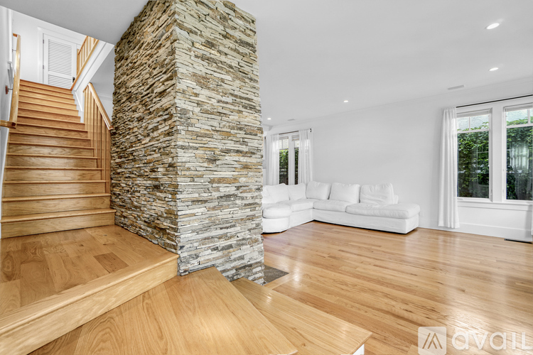 A stone pillar stands in a spacious room with wooden floors and white furniture.