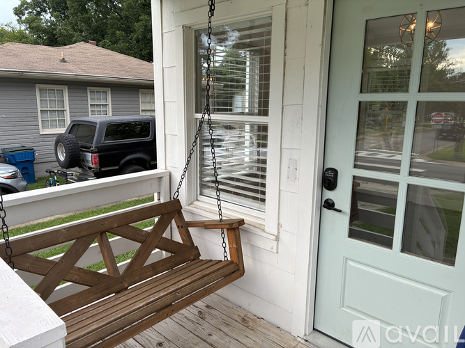 A wooden porch swing hangs from a chain on a white door.