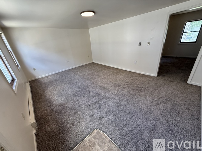 A spacious room with a carpeted floor and a window on the left side.
