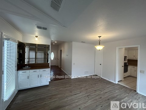 A spacious room with wooden floors and white walls, featuring a kitchen area with white cabinets and a countertop.
