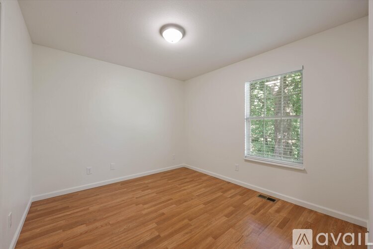 A room with wooden flooring and a window with a view of trees.