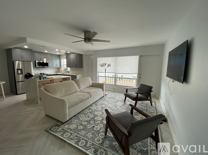 A living room with a white couch, a rug, and a flat screen TV mounted on the wall.