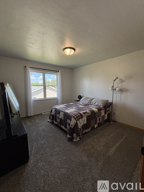 A bedroom with a bed, a window, and a carpeted floor.