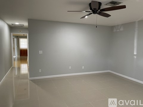 A spacious room with a ceiling fan and a doorway leading to another room.