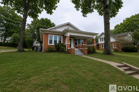 A house with a red brick exterior and a white roof is surrounded by green grass and trees.