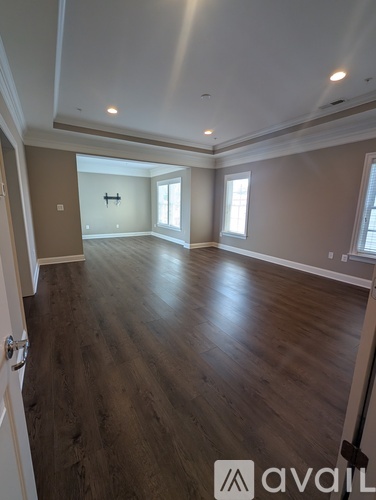 A spacious room with wooden floors and a door on the left.