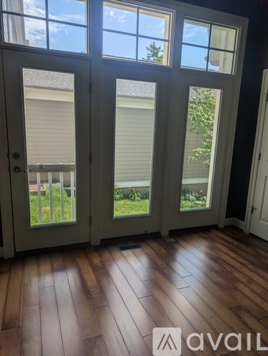 A room with a wooden floor and a large door with a view of a house and trees outside.