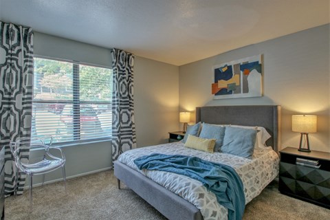 A bedroom with a bed, chair, and window with curtains.
