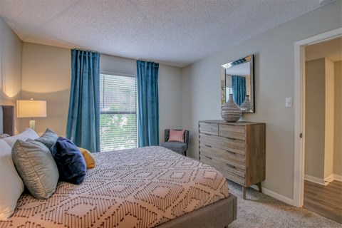 A bedroom with a bed, dresser, and window with blue curtains.