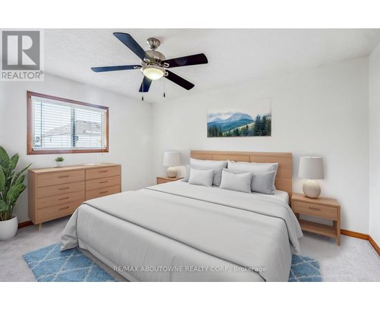 A bedroom with a large bed, a ceiling fan, and a painting of a mountain landscape on the wall.