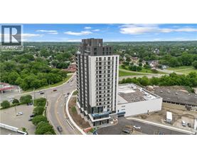 A tall building with a balcony on the top floor is surrounded by greenery and roads.
