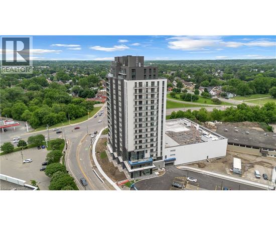 A tall building with a balcony on the top floor is surrounded by greenery and roads.