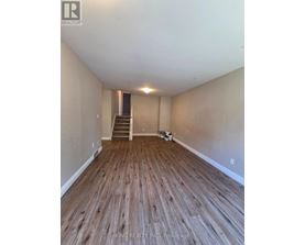 A room with wooden flooring and a staircase in the background.