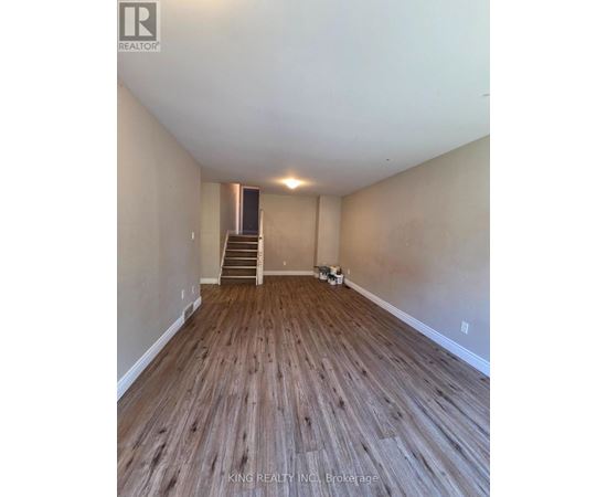 A room with wooden flooring and a staircase in the background.