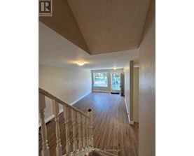A hallway with wood floors and white railings leading to a door.