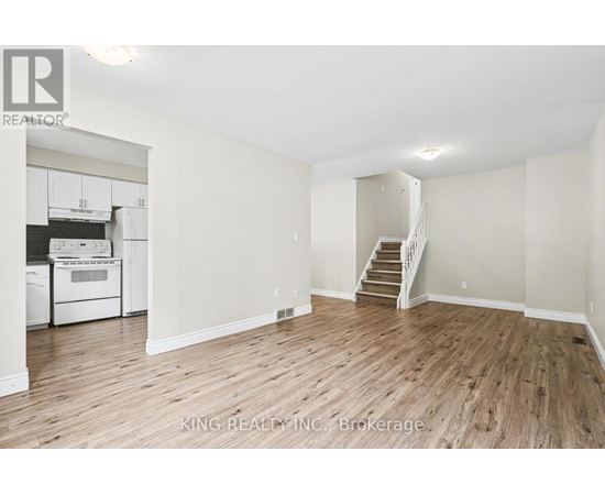 A spacious room with wooden flooring and a staircase leading to another room.