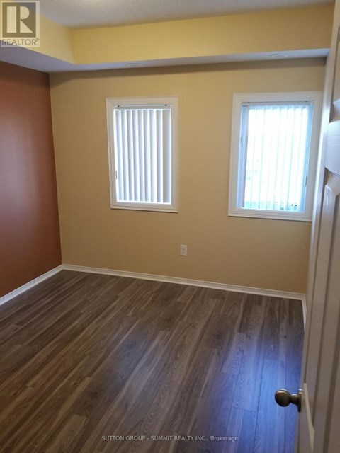 A room with wooden flooring and two windows.