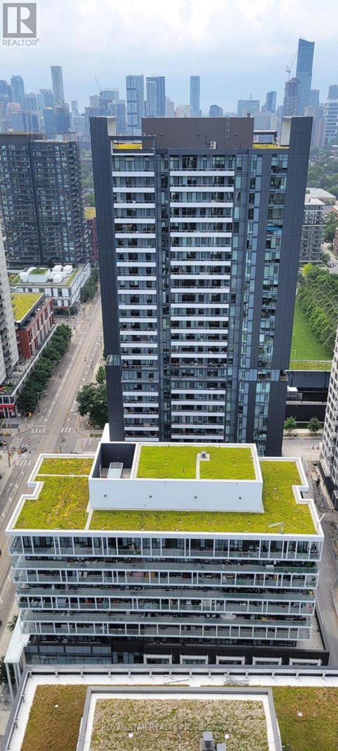 A tall building with a green roof is surrounded by other buildings.