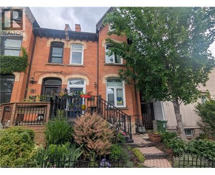 A red brick house with a black iron fence and a green trash can.