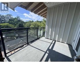A balcony with a glass railing and a view of trees and a parking lot.