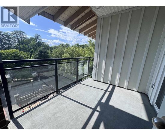 A balcony with a glass railing and a view of trees and a parking lot.