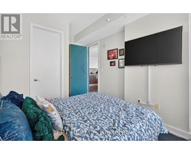 A bedroom with a bed, a blue door, and a black TV mounted on the wall.