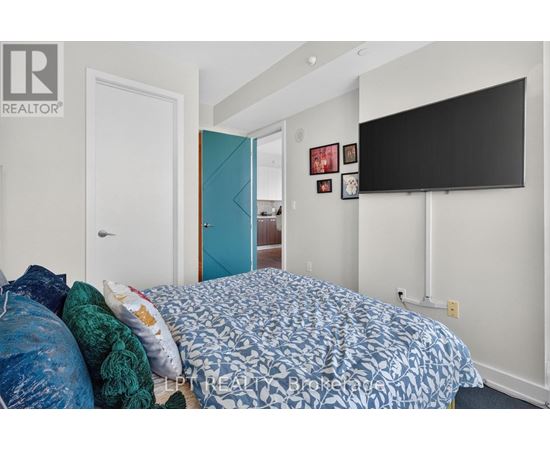 A bedroom with a bed, a blue door, and a black TV mounted on the wall.