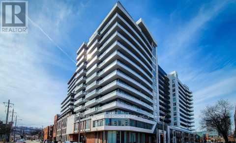 A tall, modern building with many windows and balconies is shown under a clear blue sky.