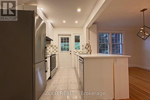 A modern kitchen with a refrigerator on the left and a countertop with a window in the background.