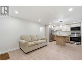 A well-lit, modern kitchen and living room with a beige sofa and wooden flooring.