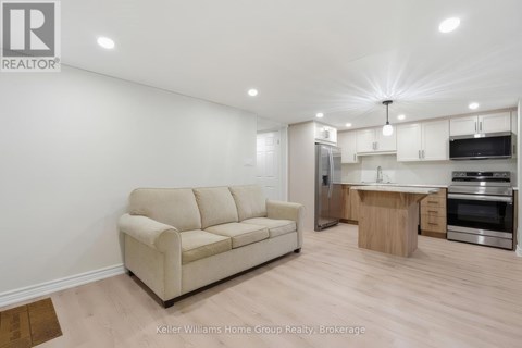 A well-lit, modern kitchen and living room with a beige sofa and wooden flooring.