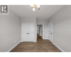 A spacious room with white walls and wooden flooring, featuring a row of white doors.